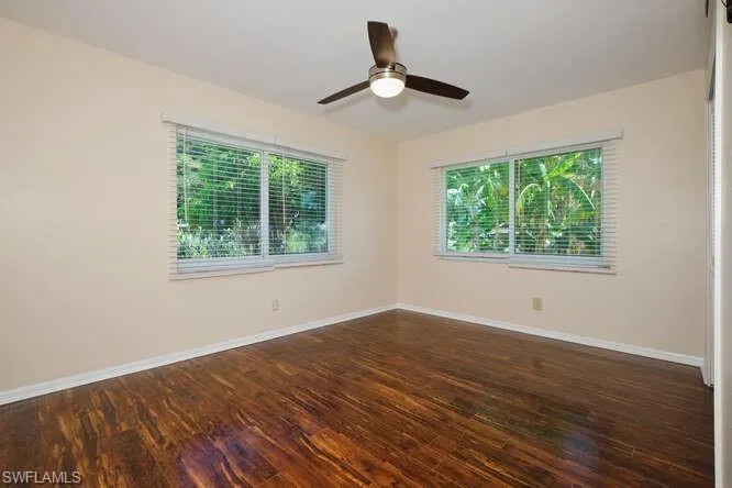 Spare room featuring dark wood-type flooring, a healthy amount of sunlight, and ceiling fan