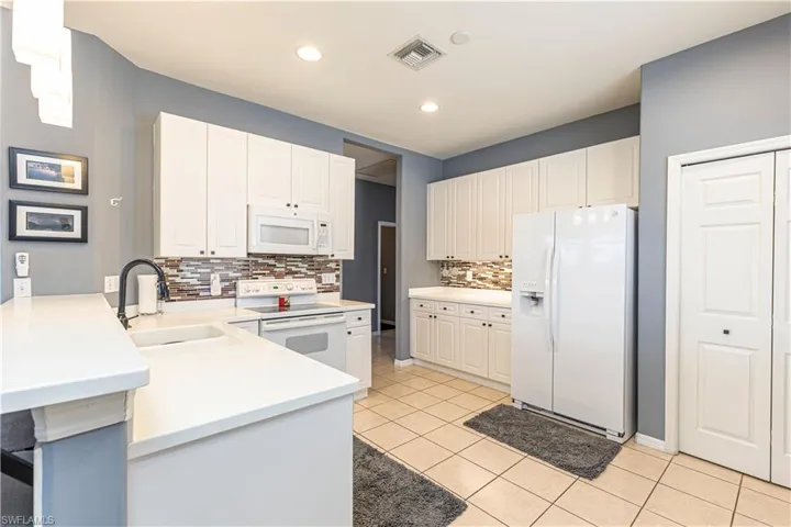 Kitchen featuring white cabinets, decorative backsplash, white appliances, and light tile floors