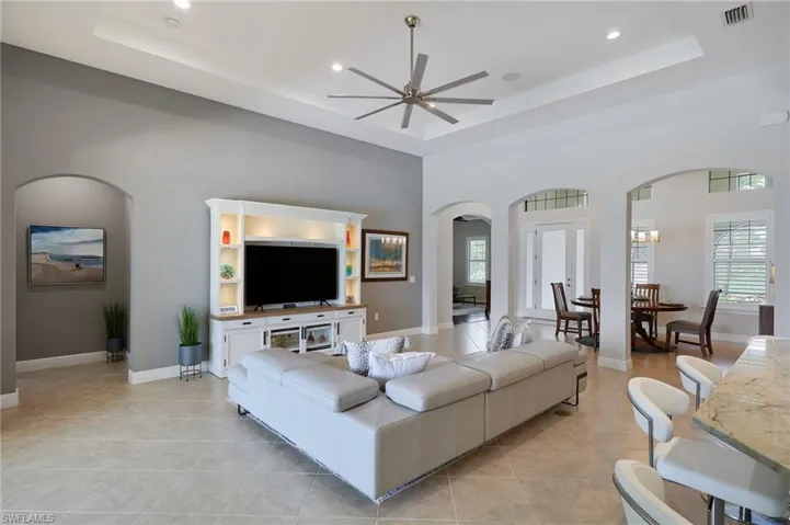 Living area with arched walkways, ceiling fan, a raised ceiling, healthy amount of natural light, and recessed lighting