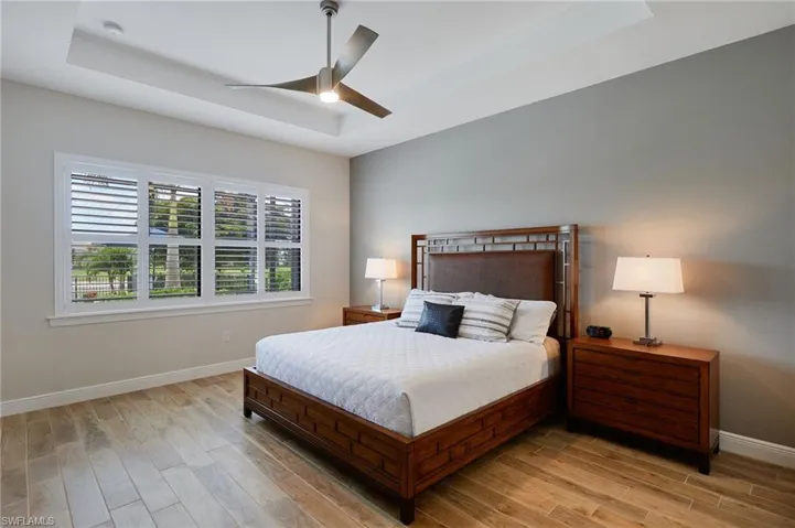 Bedroom featuring a raised ceiling, baseboards, light wood-style floors, and a ceiling fan