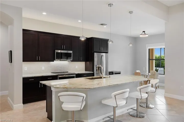 Kitchen with appliances with stainless steel finishes, a sink, a kitchen bar, backsplash, and a center island with sink