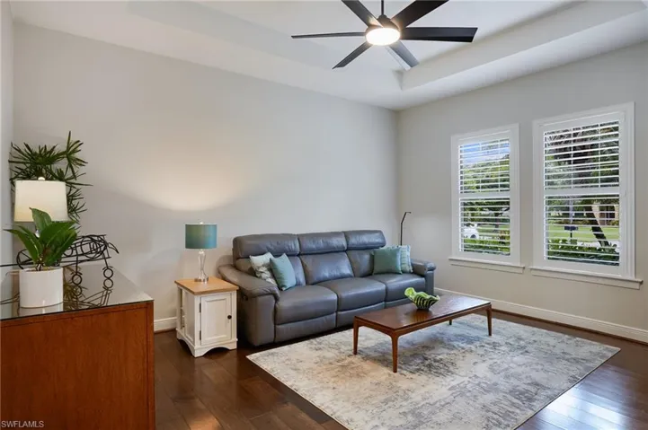 Living room featuring a ceiling fan, dark wood-style floors, baseboards, and a tray ceiling