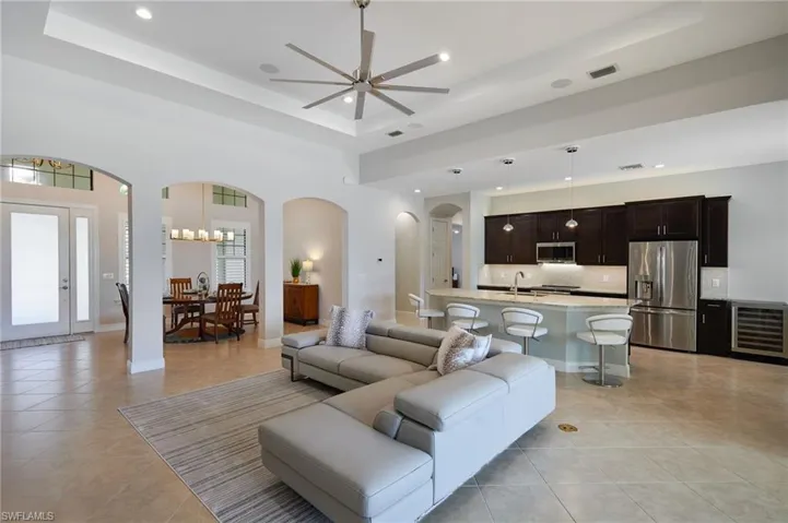 Living room with a tray ceiling, arched walkways, ceiling fan, light tile patterned floors, and recessed lighting