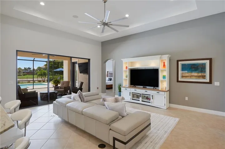 Living room featuring a raised ceiling, a ceiling fan, light tile patterned floors, arched walkways, and recessed lighting