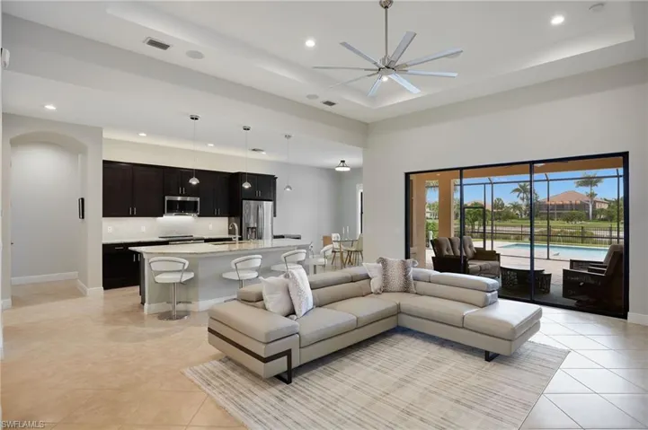 Living area with recessed lighting, a raised ceiling, a ceiling fan, light tile patterned flooring, and baseboards