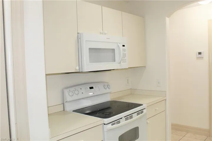 Kitchen with white appliances, light countertops, arched walkways, light tile patterned floors, and cream cabinetry