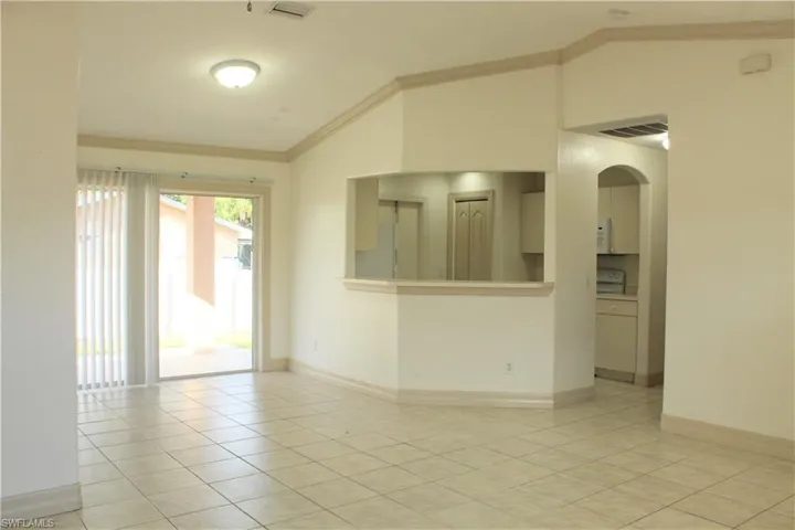 Unfurnished room featuring lofted ceiling, crown molding, arched walkways, and light tile patterned floors
