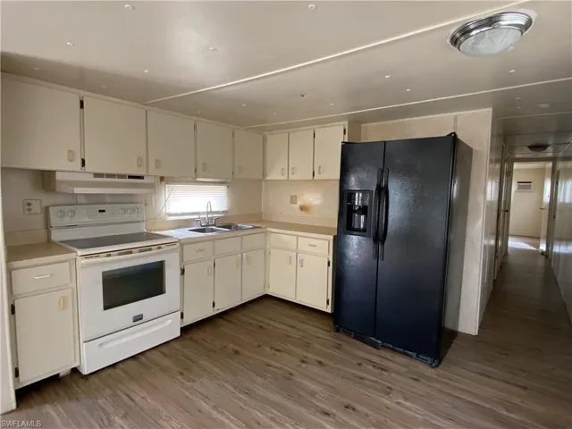 Kitchen with electric range, black refrigerator with ice dispenser, light countertops, dark wood-type flooring, and white cabinets