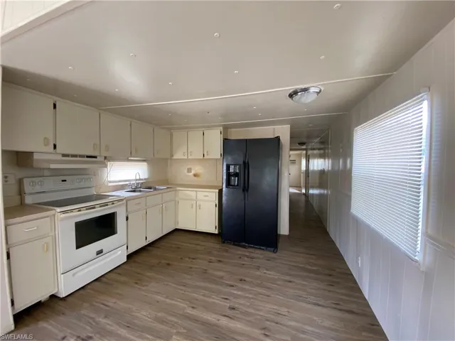 Kitchen with electric stove, black refrigerator with ice dispenser, light countertops, and dark wood-style floors