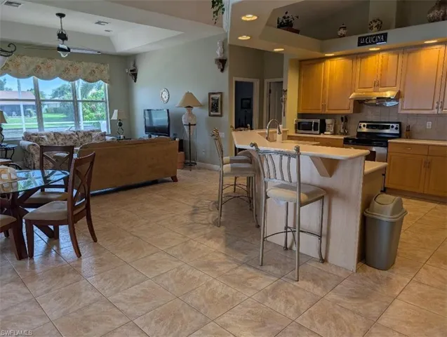 Kitchen featuring appliances with stainless steel finishes, light countertops, tasteful backsplash, open floor plan, and a kitchen breakfast bar