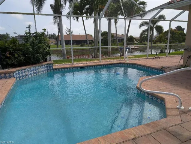 Swimming pool featuring glass enclosure, a water view, and a patio