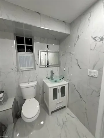 Bathroom with vanity, stone wall, and light marble finish floors