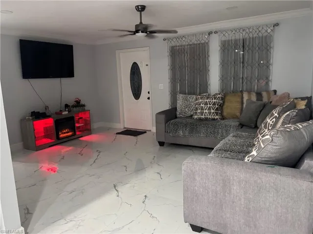 Living room with ornamental molding, a ceiling fan, and light marble finish floors