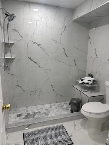 Bathroom featuring stone wall, marble tiled floors, a marble finish shower, and tile walls