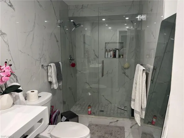 Bathroom with a marble finish shower, light marble finish floors, tile walls, vanity, and stone wall