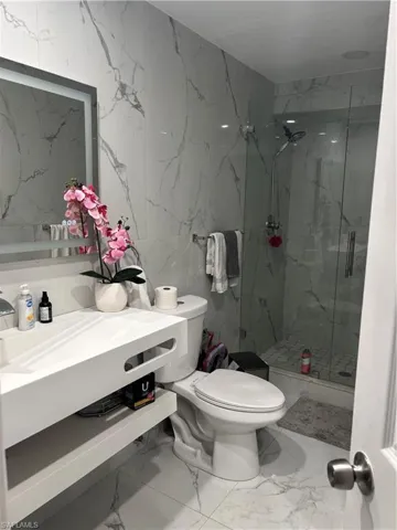 Bathroom with stone wall, a marble finish shower, light marble finish flooring, vanity, and tile walls