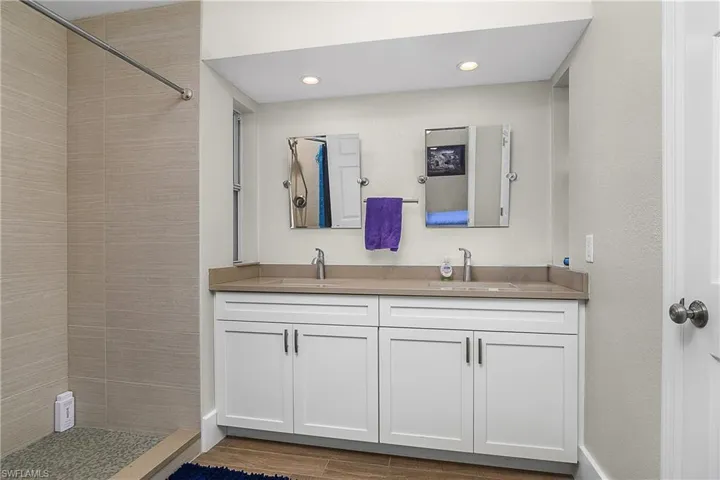 Full bathroom featuring tiled shower, double vanity, a sink, and wood finished floors