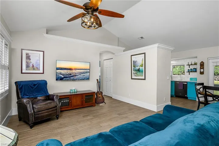 Living room featuring vaulted ceiling, a ceiling fan, light wood-style floors, visible vents, and arched walkways