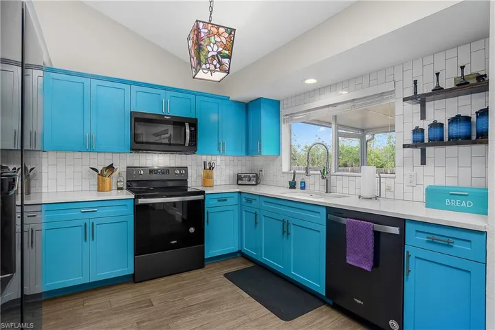 Kitchen featuring dishwashin, vaulted ceiling, blue cabinets, a double sink, and range with electric cooktop