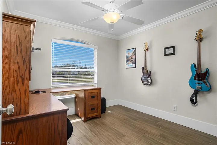 Office space featuring baseboards, light wood-type flooring, crown molding, and ceiling fan
