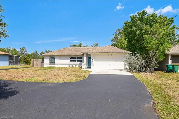 Ranch-style home with a garage, driveway, stucco siding, and a large front lawn