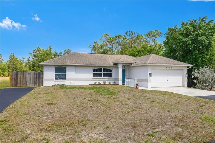 Ranch-style house featuring an attached garage, concrete driveway, stucco siding, and a front lawn