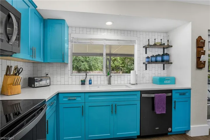 Kitchen featuring stainless steel microwave, dishwashing machine, blue cabinetry, and decorative backsplash