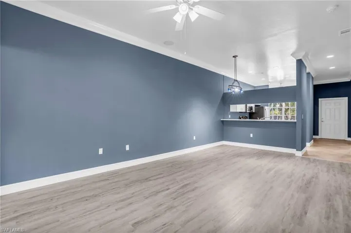 Unfurnished living room with ceiling fan, light wood-type flooring, and ornamental molding