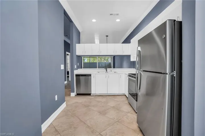 Kitchen featuring crown molding, light tile patterned floors, white cabinets, stainless steel appliances, and sink