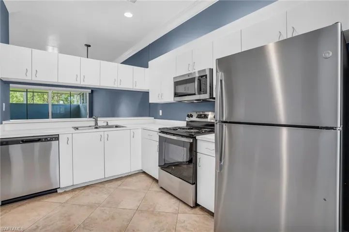 Kitchen with appliances with stainless steel finishes, white cabinets, sink, light tile patterned floors, and ornamental molding