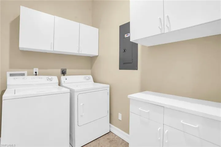Clothes washing area featuring cabinets, electric panel, independent washer and dryer, and light tile patterned flooring