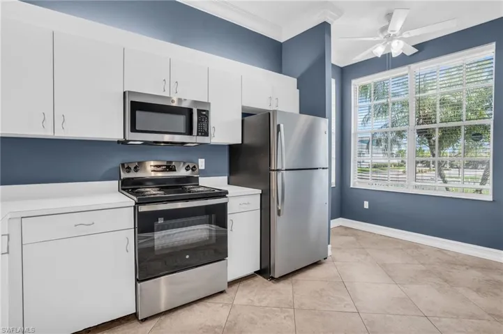 Kitchen with appliances with stainless steel finishes, white cabinets, light tile patterned floors, ceiling fan, and ornamental molding