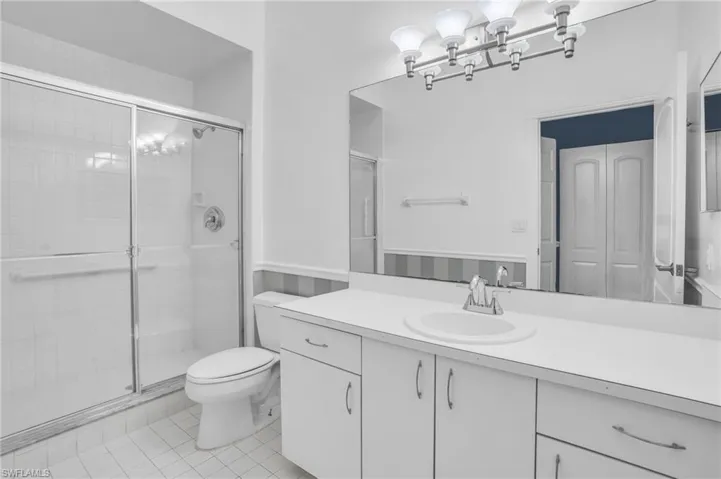 Bathroom with a shower with shower door, vanity, tile patterned floors, and toilet