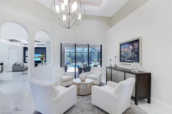 Living room with suspended lighting, light tile flooring, and a high coffered ceiling
