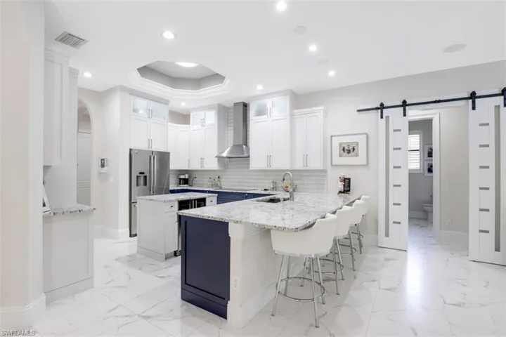 Dual tone kitchen featuring a barn door to the guest wing, a peninsula, a breakfast bar, and light granite countertops