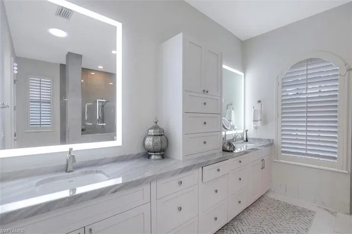Bathroom with double vanity, lighted mirrors, a walk in double shower, and light tile flooring