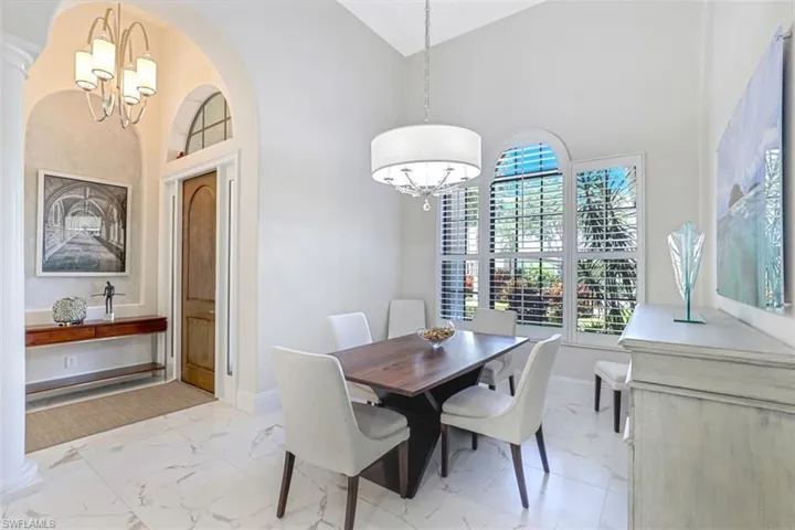 Formal Dining room with chandelier, light marble finish floors, open walkways, and vaulted ceiling.