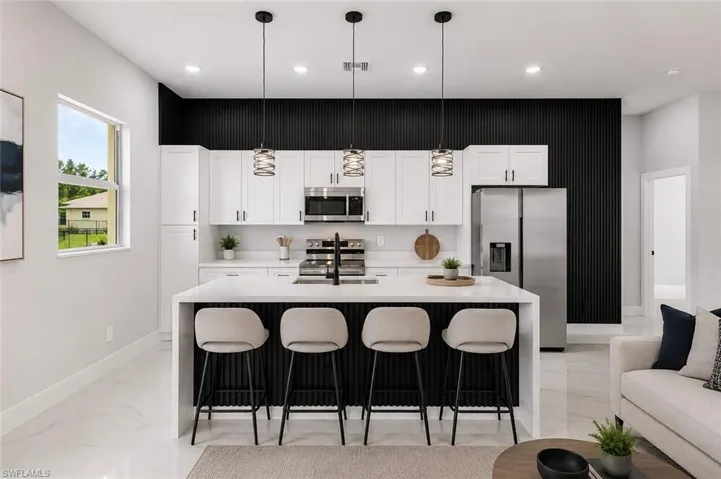 Modern kitchen featuring a waterfall island, white cabinetry, stainless steel appliances, and a black accent wall