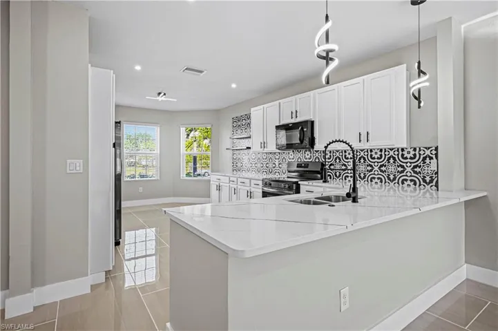 Kitchen featuring visible vents, backsplash, black microwave, stainless steel electric range oven, and a sink