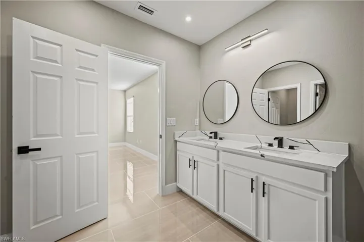 Bathroom with tile patterned flooring, double vanity, visible vents, and a sink