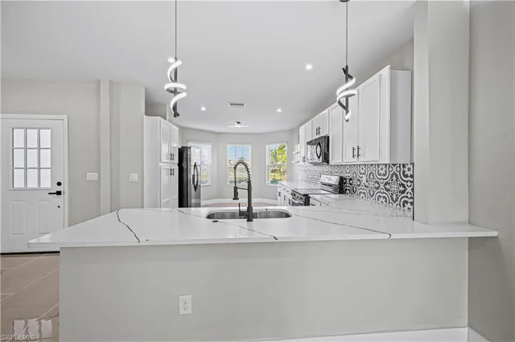 Kitchen with light stone countertops, decorative backsplash, appliances with stainless steel finishes, a peninsula, and a sink