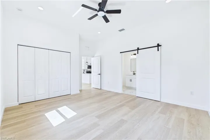 Unfurnished bedroom featuring a barn door, light wood-style flooring, a ceiling fan, a closet, and recessed lighting