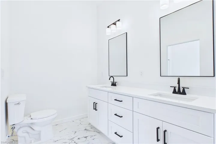 Full bath featuring double vanity and light marble finish floors