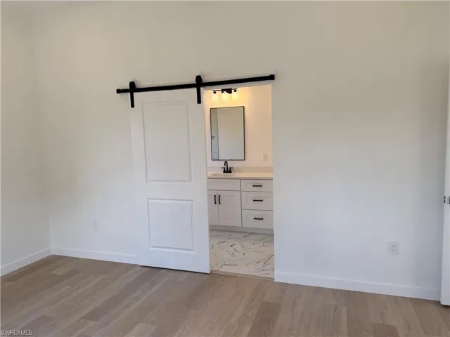 Unfurnished bedroom with a barn door, light wood-style flooring, and connected bathroom
