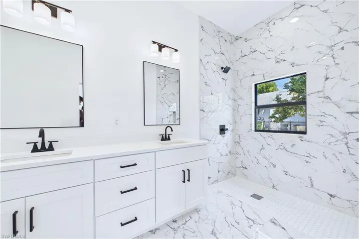 Full bath with a marble finish shower and double vanity