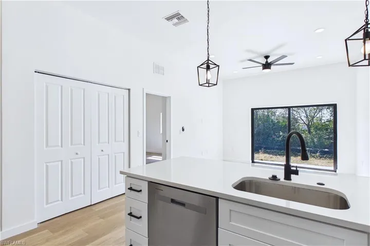 Kitchen featuring dishwasher, pendant lighting, white cabinets, and light wood-type flooring