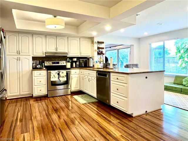 Kitchen with dark hardwood / wood-style floors, backsplash, kitchen peninsula, white cabinets, and appliances with stainless steel finishes