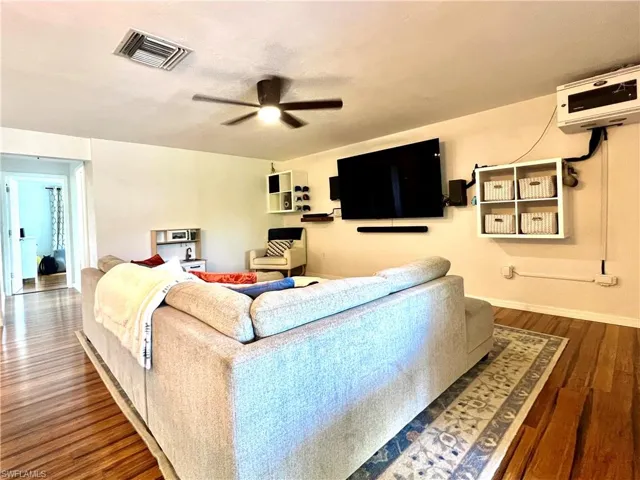 Living room featuring ceiling fan, a wall mounted air conditioner, and dark hardwood / wood-style floors