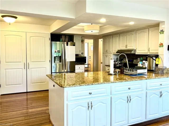 Kitchen with stone countertops, dark hardwood / wood-style flooring, white cabinetry, and appliances with stainless steel finishes