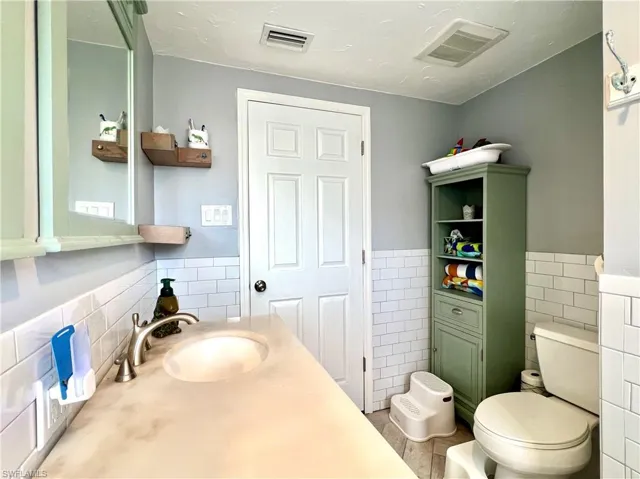 Bathroom featuring vanity, tile walls, and toilet